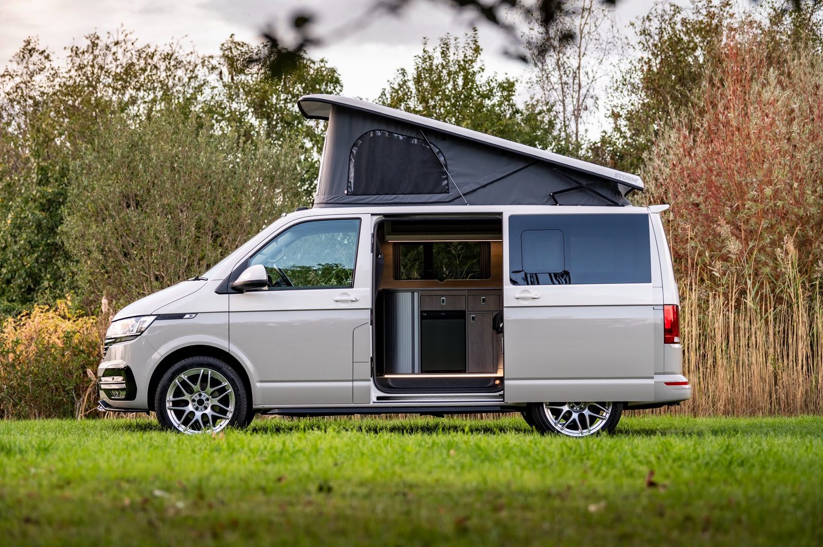 VW Transporter camper with Storm pop-top raised and side door open, showing the interior