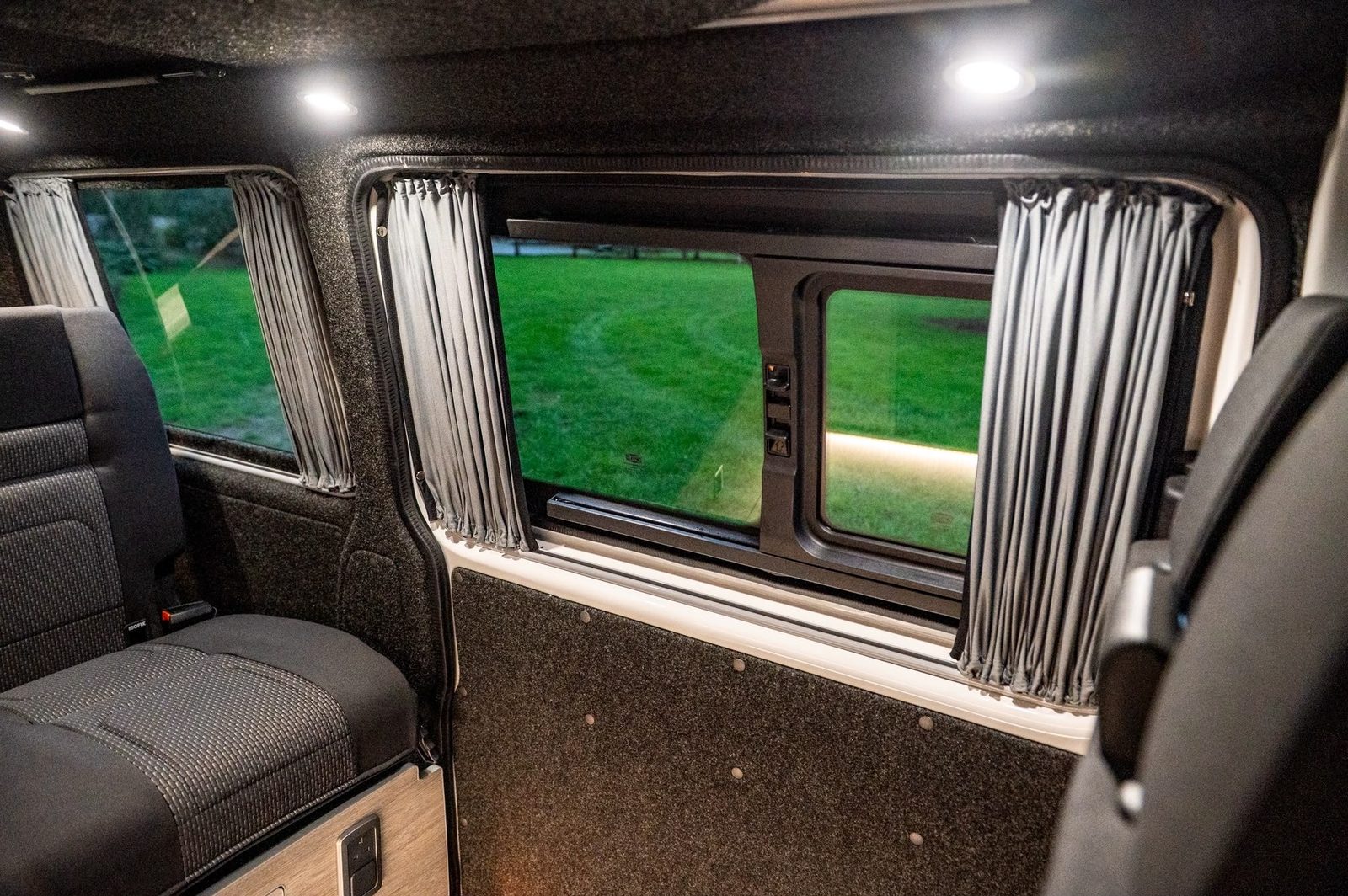 View from inside a VW Transporter camper through the side windows, with curtains fitted